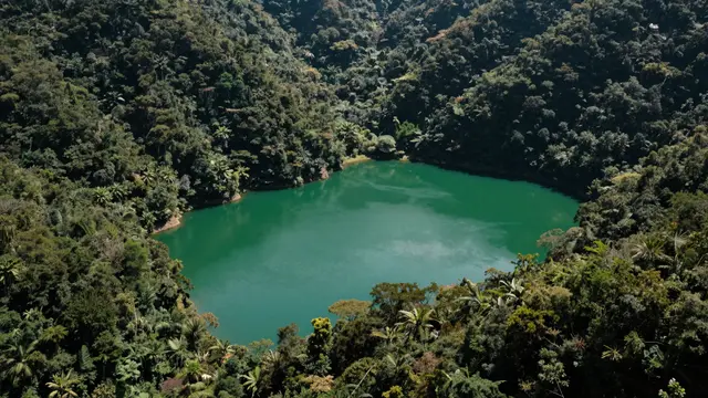 Aerial view of a vivid emerald green lake surrounded by dense steep tropical forest slopes