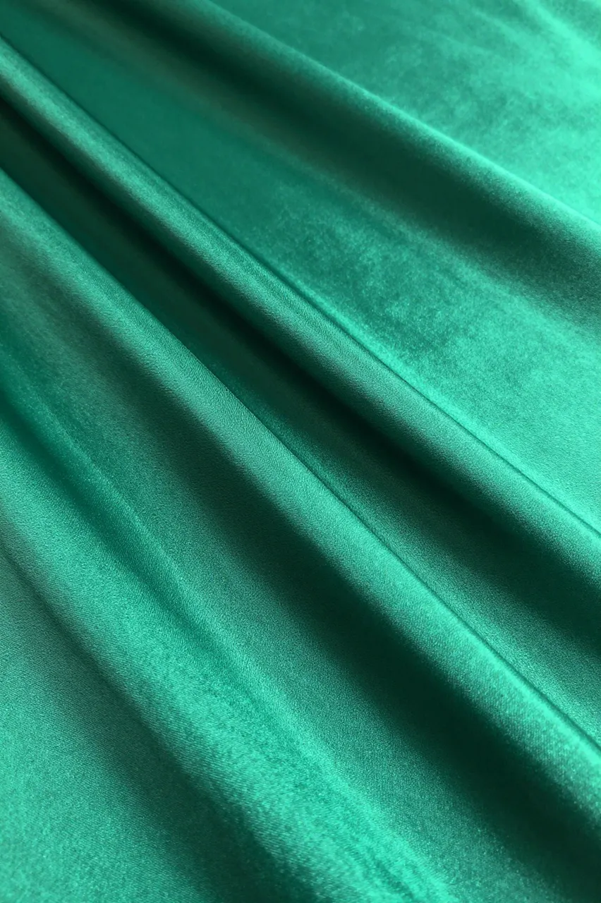 Close-up full frame of glossy gathered emerald satin with diagonal pleats and soft light reflections