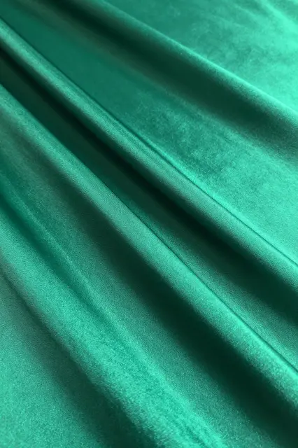 Close-up full frame of glossy gathered emerald satin with diagonal pleats and soft light reflections