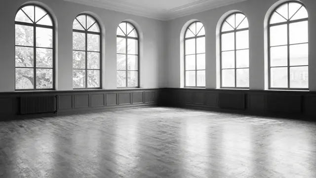 Black and white view of an empty polished ballroom with tall arched windows and pooling natural light.