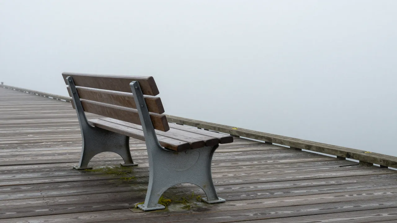 An empty wooden bench sits on a weathered wooden pier surrounded by thick fog
