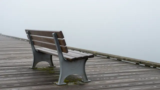 An empty wooden bench sits on a weathered wooden pier surrounded by thick fog