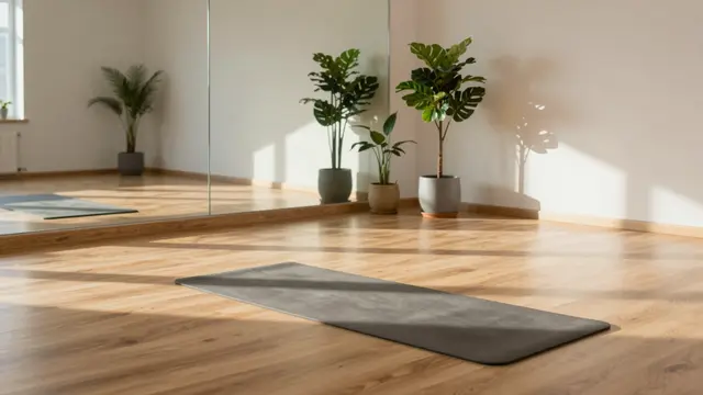 An empty yoga studio with wooden flooring, potted plants, a mirror, and a yoga mat lit by soft morning sunlight.