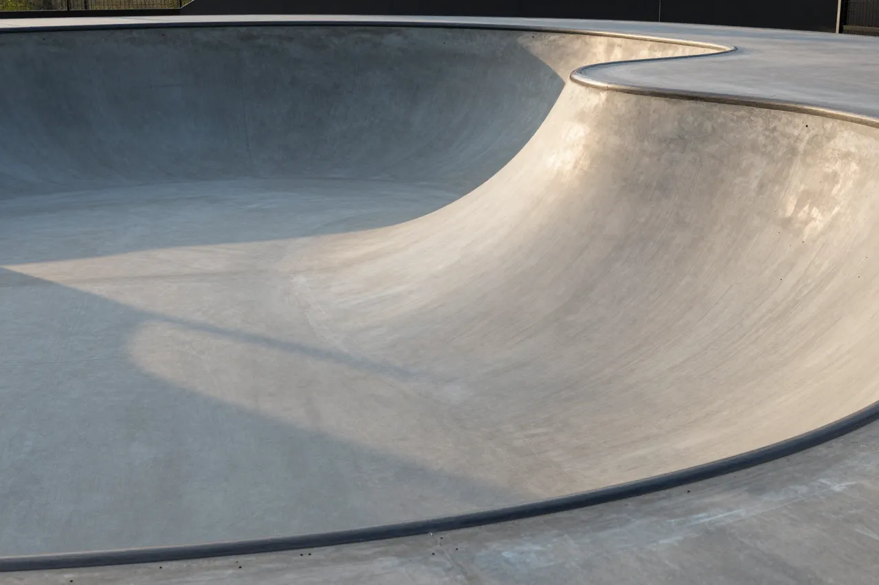 Smooth empty gray concrete skate bowl lit with warm soft sunset light casting curved shadows