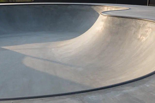 Smooth empty gray concrete skate bowl lit with warm soft sunset light casting curved shadows