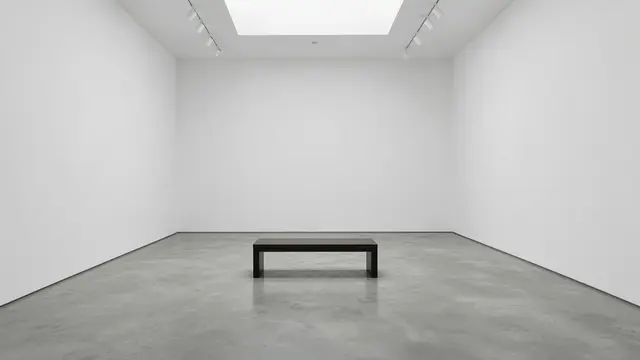 A stark empty museum gallery with blank white walls, a central dark bench, and overhead track lighting.