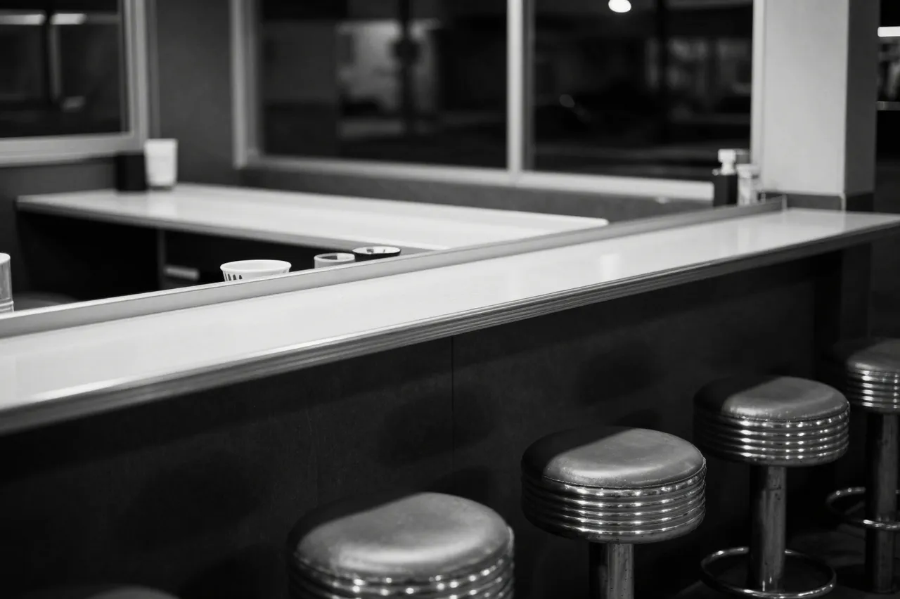 Black and white view of an empty retro diner counter with lined-up metal stools after hours
