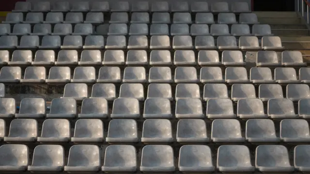 Rows of plain empty gray plastic stadium seats lit by warm evening light