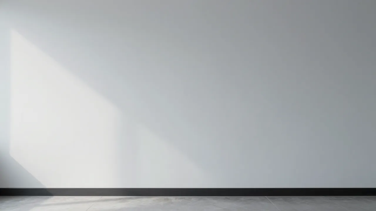 Plain light gray empty office wall with soft diagonal daylight wash from the left above a tiled floor