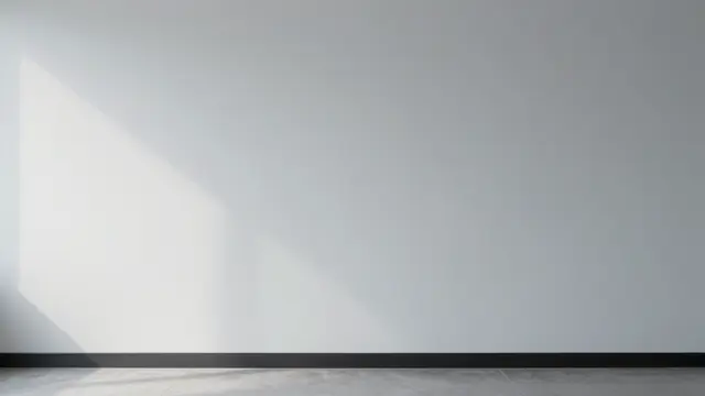 Plain light gray empty office wall with soft diagonal daylight wash from the left above a tiled floor