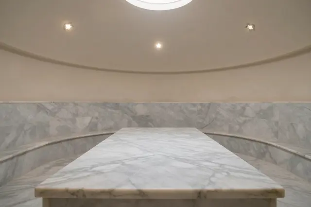 Unoccupied hammam steam room with a marble slab, domed ceiling, and small star skylights in soft haze.