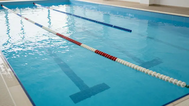 An empty indoor swimming competition pool with calm bright blue water and floating lane divider ropes