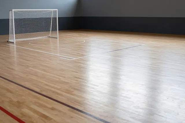 An empty polished wooden indoor futsal court with a small goal and court markings