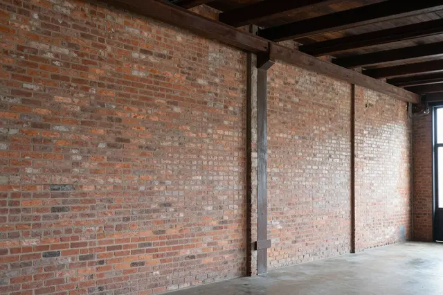 Unfurnished industrial loft with exposed red brick walls, dark wooden ceiling beams and a concrete floor
