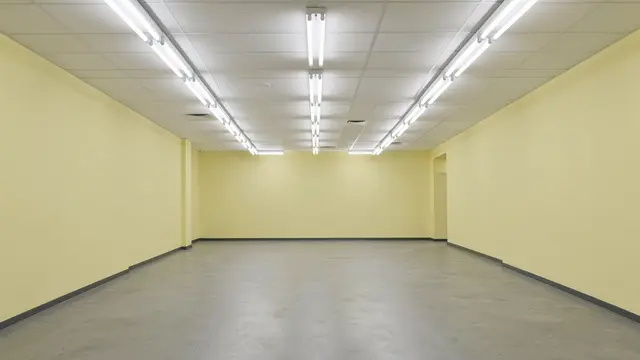 Unfurnished empty office space with pale yellow walls and rows of ceiling fluorescent lights