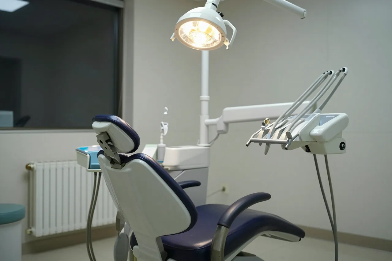 Unoccupied dental chair with an overhead lit exam lamp in a quiet dim dental office at night