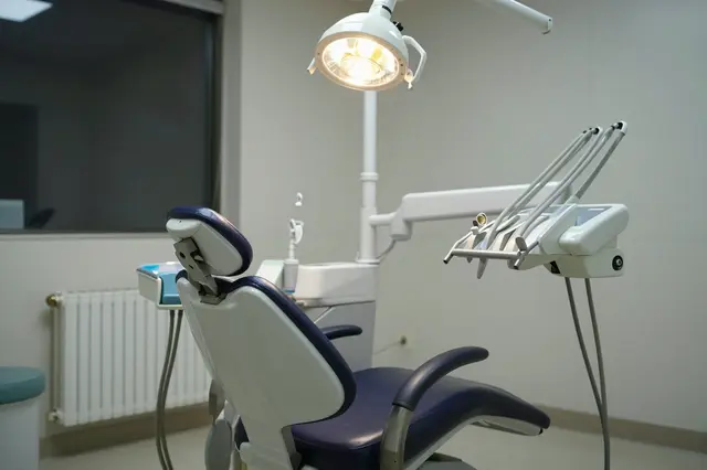 Unoccupied dental chair with an overhead lit exam lamp in a quiet dim dental office at night