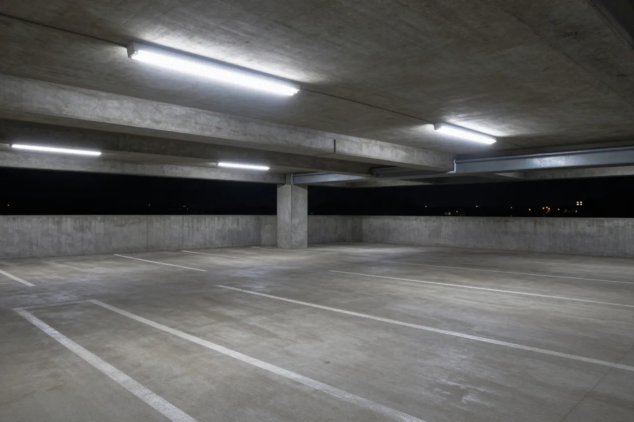 Vacant upper level concrete parking garage lit by cold fluorescent lights at night