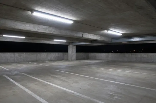 Vacant upper level concrete parking garage lit by cold fluorescent lights at night