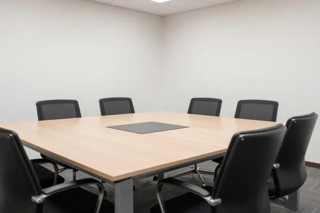Unused meeting room with a light wood table and black office chairs around it