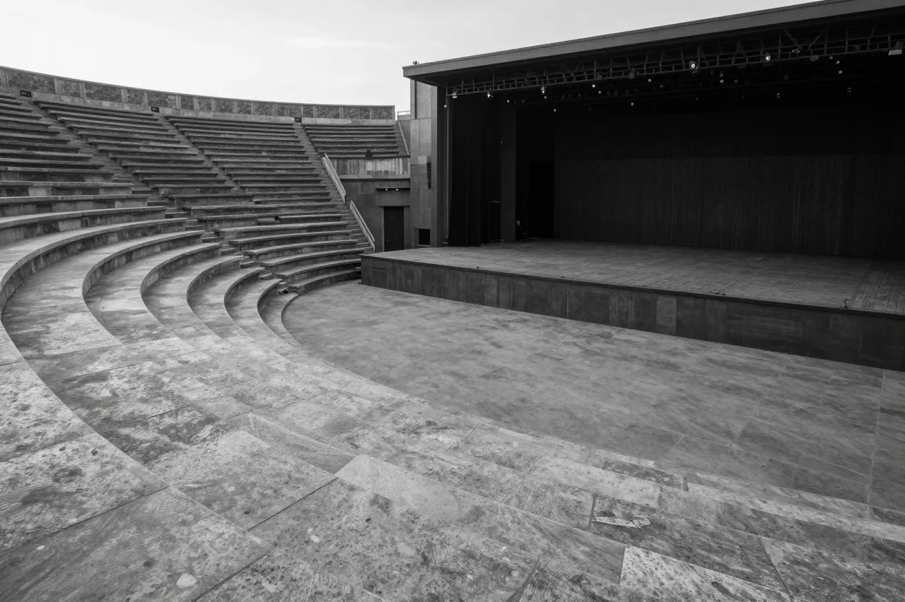 Black and white view of a vacant open-air amphitheater with curved stone seating and a bare stage at dawn