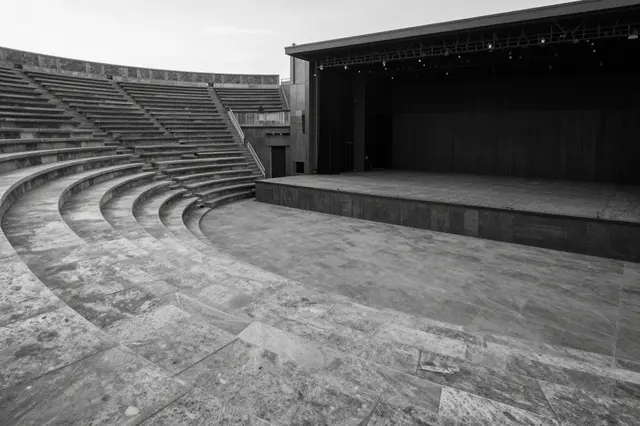 Black and white view of a vacant open-air amphitheater with curved stone seating and a bare stage at dawn