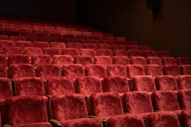 Rows of plush red velvet theater seats fill a dim empty concert hall viewed from the stage