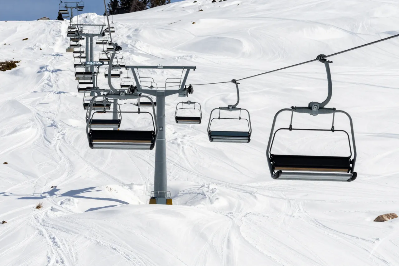 Empty ski lift chairs run up a groomed snowy mountain slope under clear sunny skies.
