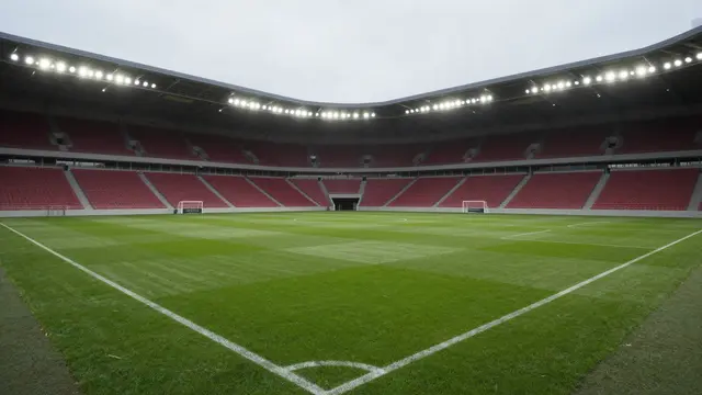 Unoccupied soccer pitch with striped grass and red seats under bright stadium floodlights