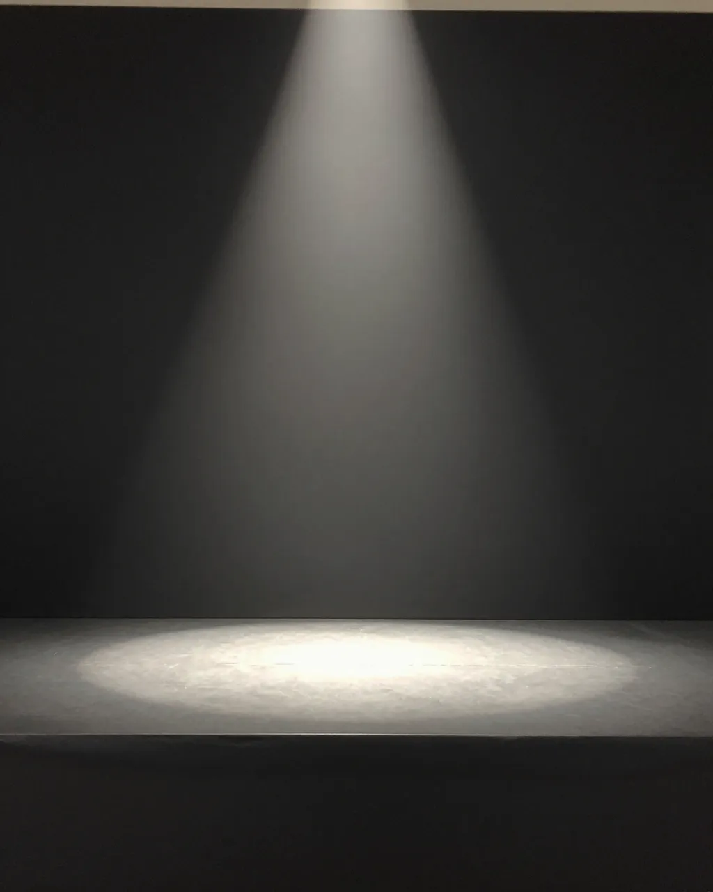 A soft downward spotlight illuminates the center of an empty matte black product stage