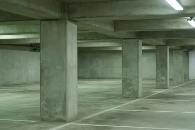 Unoccupied concrete underground parking garage with receding columns under green-tinted fluorescent lighting