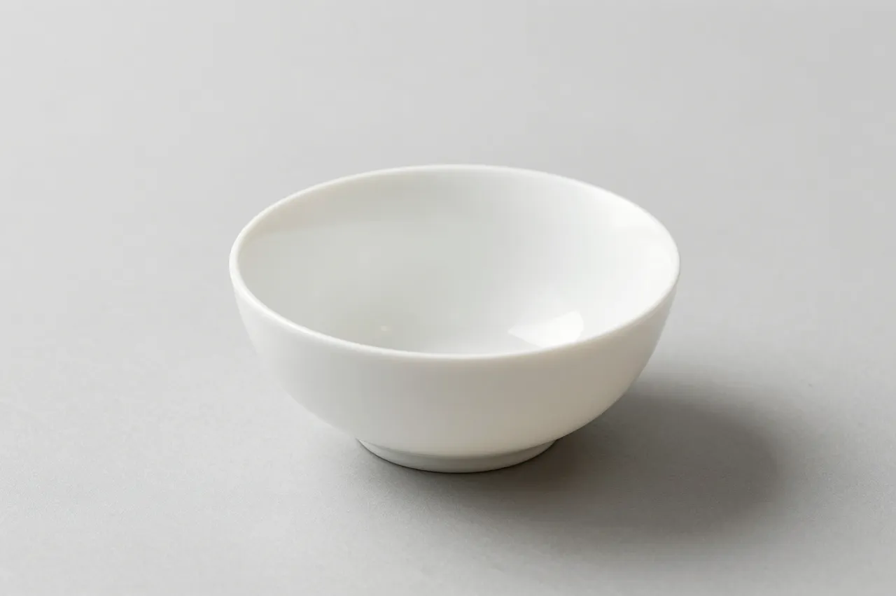 An empty glossy white ceramic bowl sits centered on a pale gray tabletop with a soft diffused shadow.