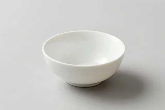 An empty glossy white ceramic bowl sits centered on a pale gray tabletop with a soft diffused shadow.