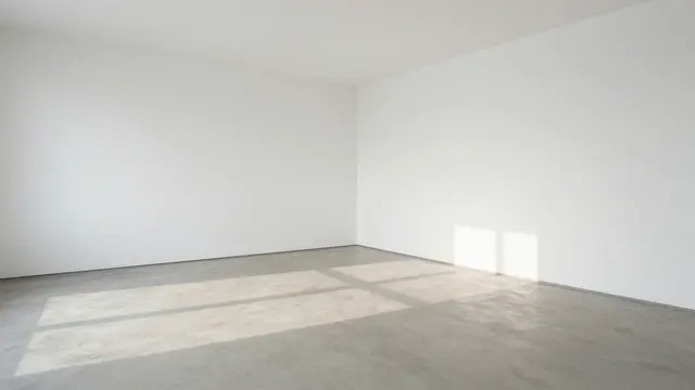 An empty minimalist gallery room with white walls, pale concrete floor and soft window daylight casting cross shadows