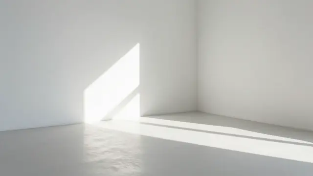 Soft diagonal sunlight falls across the floor of an empty plain white room corner with ample copy space