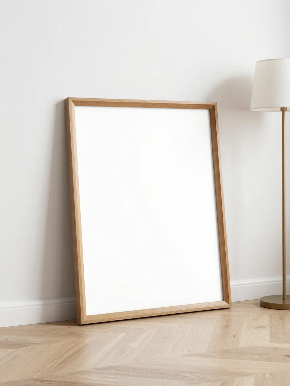 Blank wooden picture frame leans against a white wall next to a floor lamp on pale oak flooring