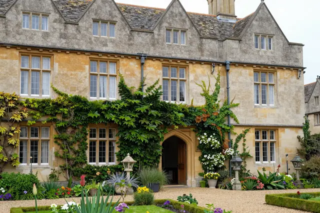 Traditional stone English manor house covered in climbing ivy fronted by a formal planted garden