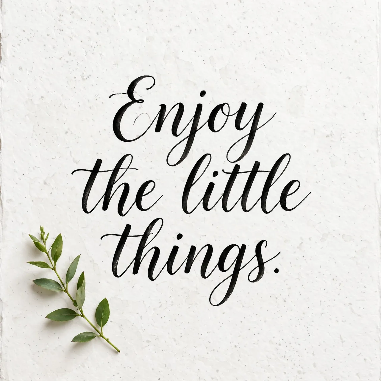 Black brush lettering reading "Enjoy the little things." sits with a small green leaf sprig on textured white watercolor