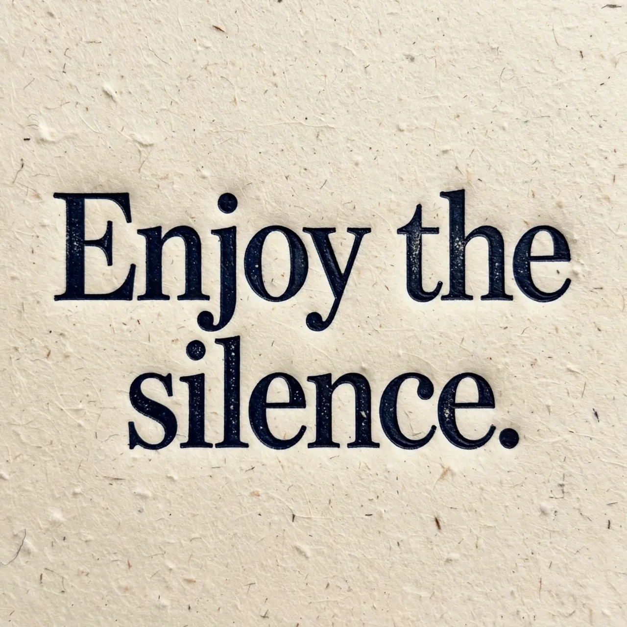 Letterpress print of the text "Enjoy the silence." in deep navy ink on textured cream cotton paper.