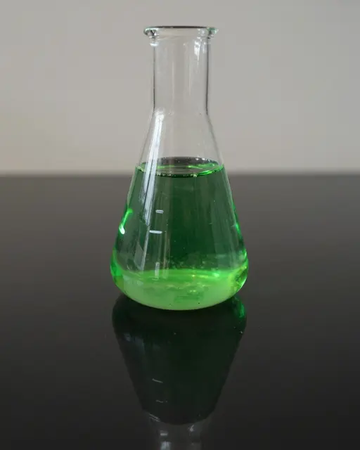 A clear conical Erlenmeyer flask holding glowing green liquid rests on a reflective black glass table