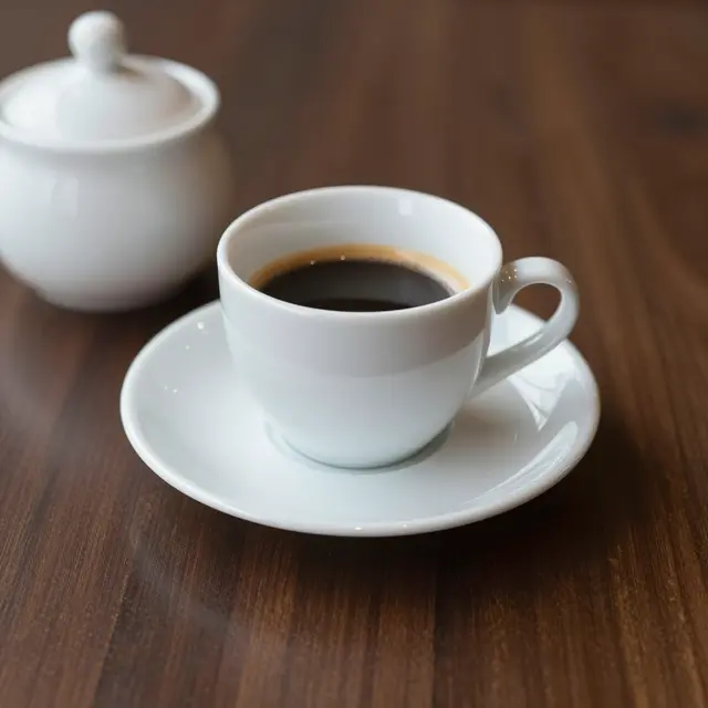 White espresso cup on a matching saucer sits beside a lidded sugar bowl on a dark walnut table.