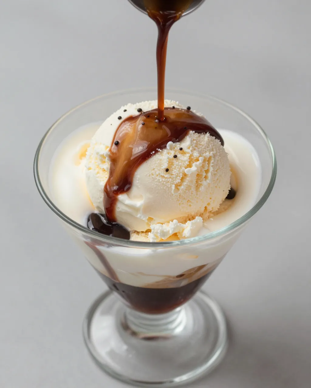 Dark espresso is poured from a spoon over a scoop of vanilla ice cream in a glass dessert cup