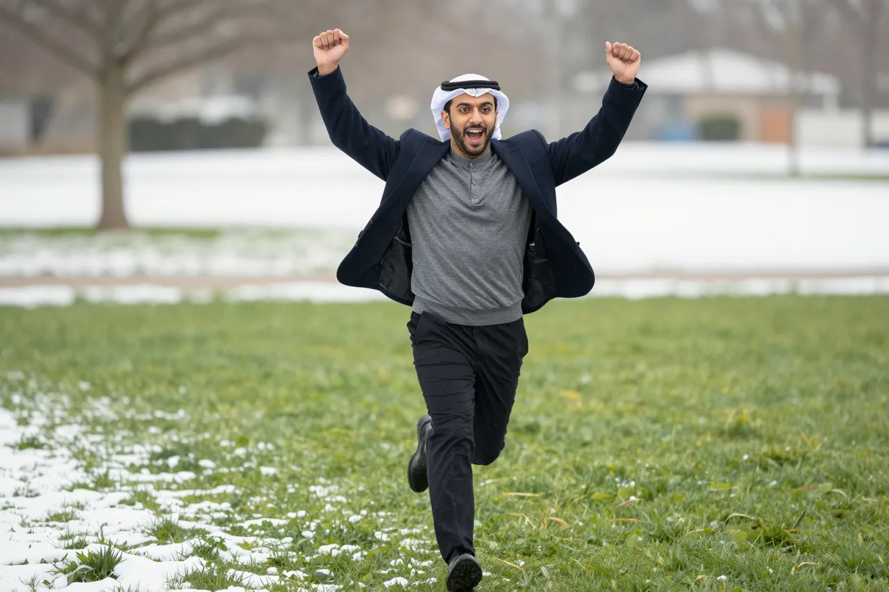 An excited Middle Eastern man runs toward the camera with raised fists on a snowy winter lawn.