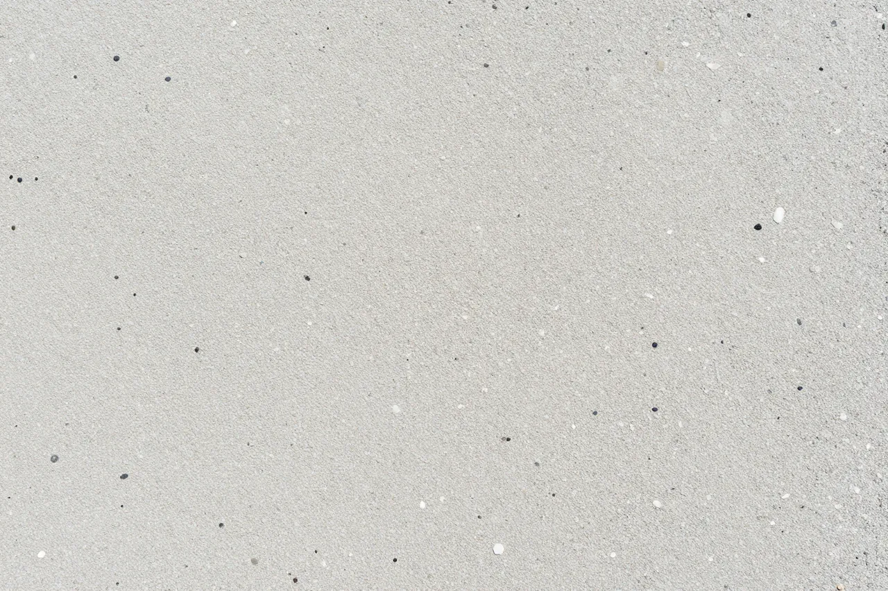 Top-down close-up of smooth light gray exposed aggregate concrete dotted with small pebbles