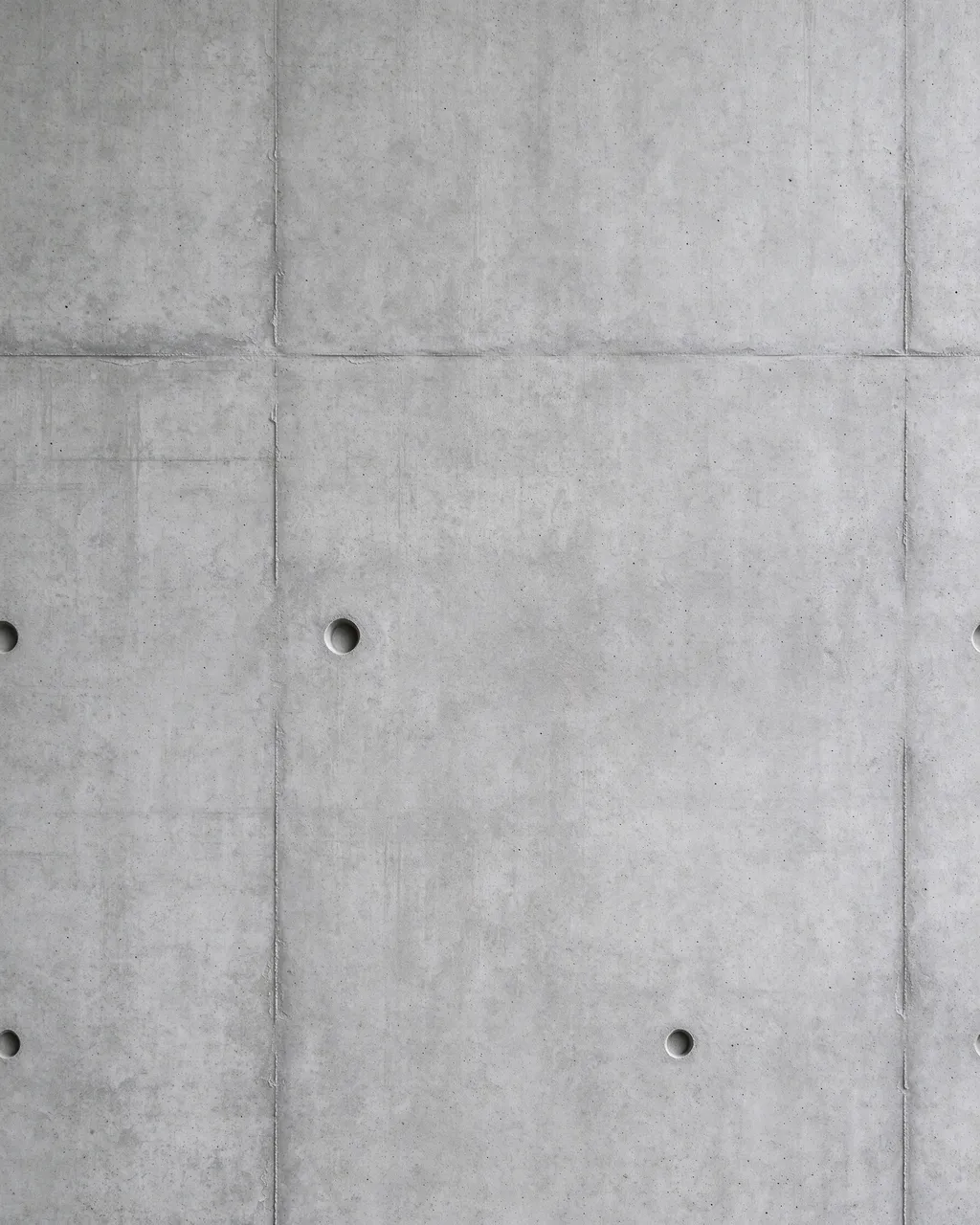 Full frame close-up of smooth cast concrete wall panels with form seams and bolt holes under flat even light