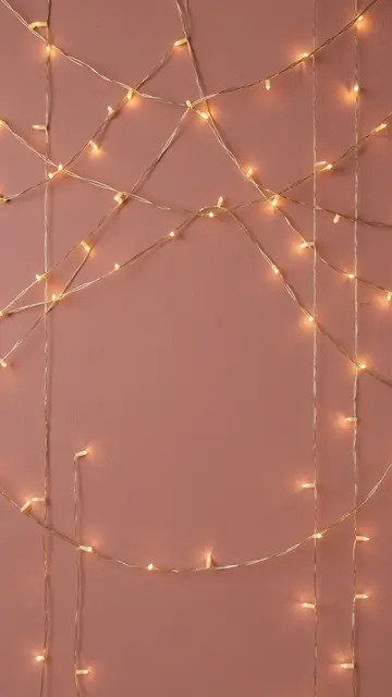 Warm golden fairy lights drape in loops over a dusty rose wall with blank central copy space