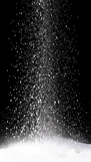 Vertical streaking falling snow appears against a solid black background, thinning toward the bottom above bright white