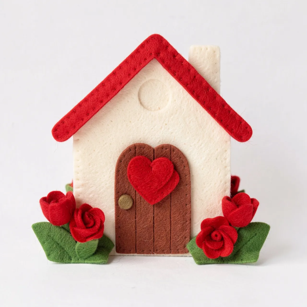 Handmade felt craft house with heart door and red felt flowers on a plain white background