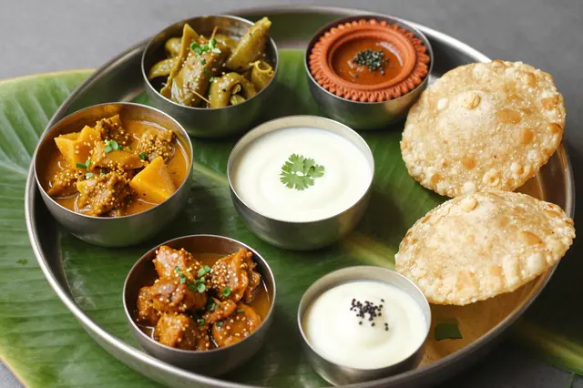 Top view of a Diwali thali on a banana leaf holding curries, fried breads, and accompaniments