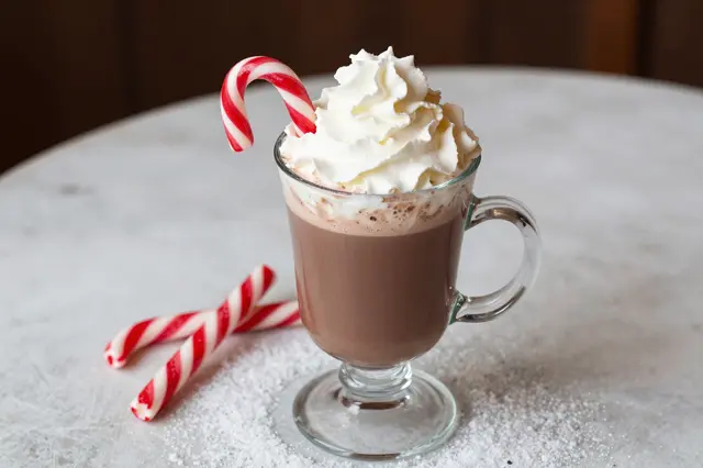 Glass mug of hot chocolate topped with whipped cream and candy canes on a snowy tabletop